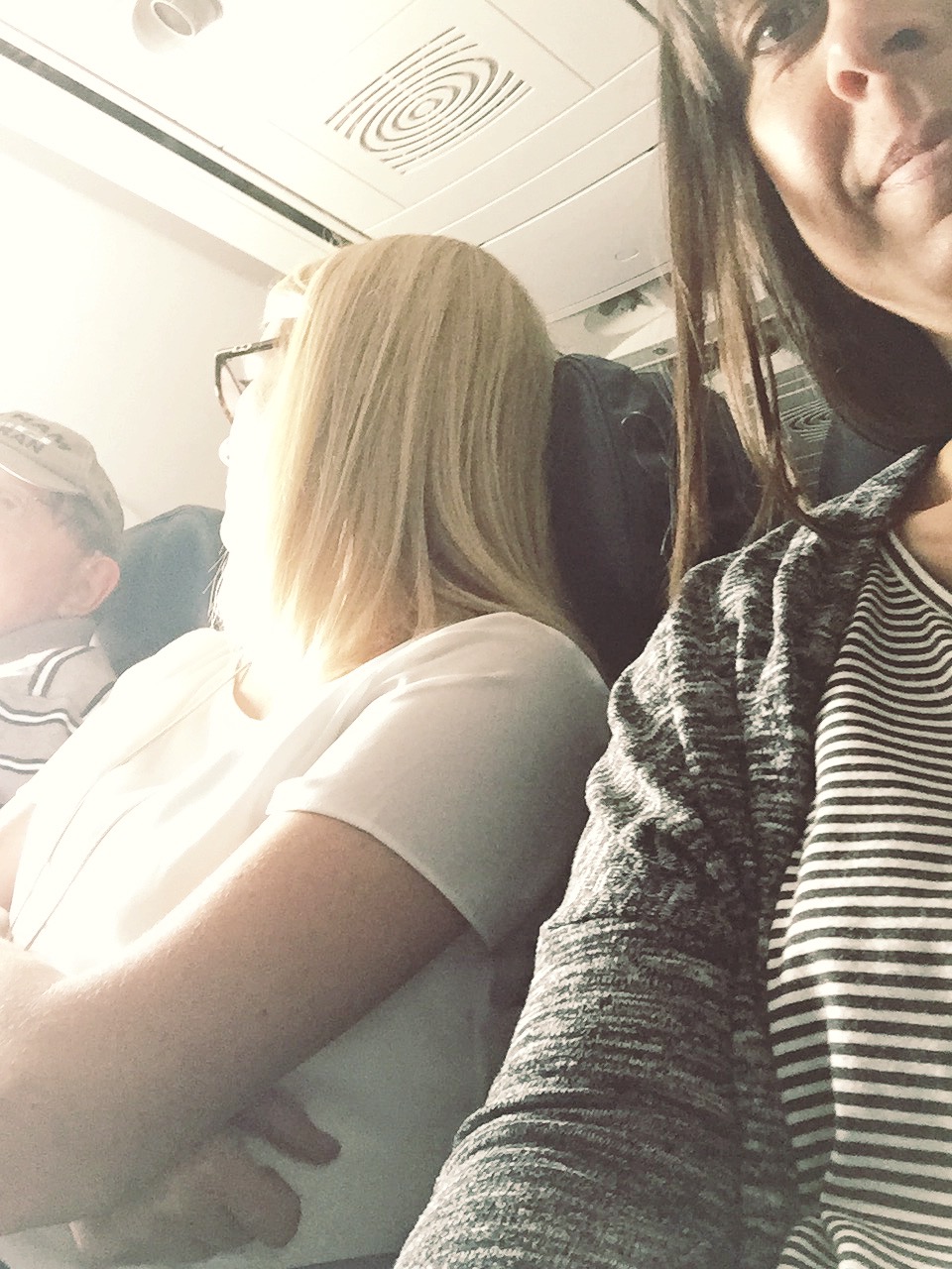woman taking picture of her friend being kind to an older gentlemen during a flight