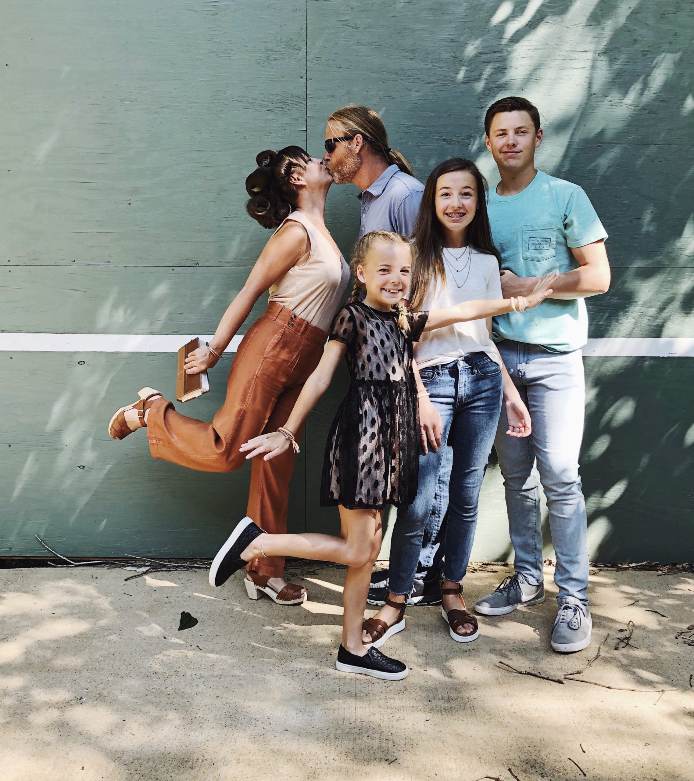 family picture in front of tennis wall with kids and mom and dad kissing